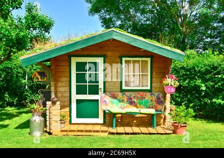 Un petit hangar en bois et vert clair, un jardin, avec un banc quelques outils autour Banque D'Images