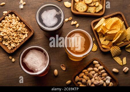Boissons artisanales dans des verres et des pistaches, noix, craquelins, chips et chips dans l'assiette et éparpillées sur une table en bois Banque D'Images