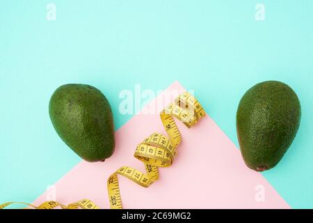 fruit vert avocat et ruban de mesure jaune torsadé sur fond rose vert, concept de régime et de perte de poids, vue du dessus Banque D'Images