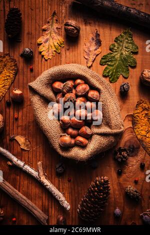 Vue de dessus des noisettes décortiquées dans un sac en toile écologique sur une table en bois rustique décorée de feuilles et de branches d'automne sèches Banque D'Images