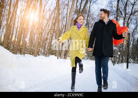 portrait de jeune heureux couple caucasien en manteaux à l'extérieur. homme et femme émotif aiment passer du temps ensemble, marcher et sauter dans la rue. r Banque D'Images