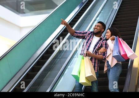 Concept de vente. Un couple noir heureux avec des sacs de shopping sur l'escalier roulant Banque D'Images