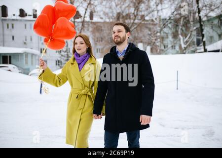 jeune et beau couple caucasien ayant la promenade. romantique homme et femme en manteaux datant, tenir les ballons d'air rouges dans les mains, ils semblent heureux togethe Banque D'Images