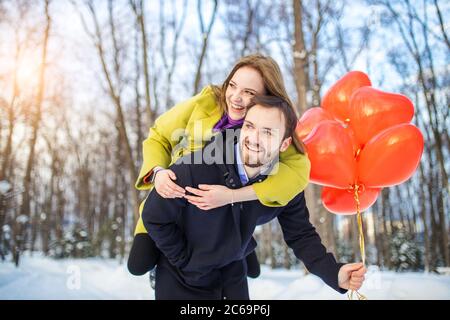 couple ayant promenade. romantique homme et femme en manteaux datant, tenir les ballons d'air rouges dans les mains, ils ont l'air heureux ensemble. belle dame a sauté sur m Banque D'Images