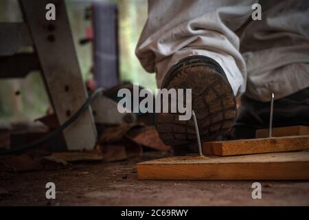 Travailleur dans des chaussures de sécurité qui marche sur des clous à bord de bois dans la zone de construction Banque D'Images