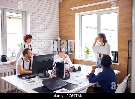 Un jeune leader asiatique couronné de succès portant des vêtements blancs et tenant un ordinateur portable prononce un discours pour un groupe de personnes multiethniques Banque D'Images