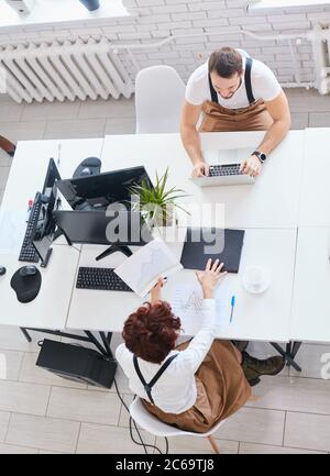 Vue de dessus sur l'équipe travaillant sur un ordinateur portable assis dans le bureau, intérieur blanc. Travail moderne, affaires pour les personnes Banque D'Images