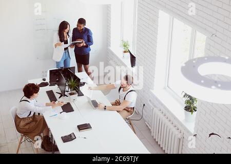 Les partenaires d'affaires étrangers se réunissent dans un bureau avec intérieur blanc. Vue de dessus sur les hommes d'affaires Banque D'Images