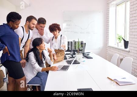 Groupe multiethnique réuni pour examiner l'ordinateur portable pour discuter du projet, divers employés se sentent euphoriques pour atteindre ensemble un objectif partagé Banque D'Images