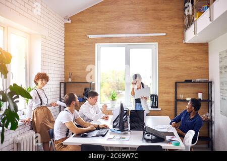 Un jeune leader asiatique couronné de succès portant des vêtements blancs et tenant un ordinateur portable prononce un discours pour un groupe de personnes multiethniques Banque D'Images