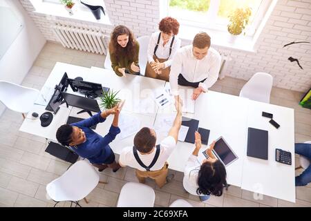 Une équipe d'affaires réussie après la réunion s'assoit autour de la table pendant que les dirigeants se secouent la main. Rencontre internationale, partenariat multiethnique. Vue de dessus Banque D'Images