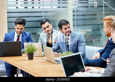 Les jeunes politiciens mènent des négociations sur un nouveau projet, un nouveau contrat, en utilisant des ordinateurs portables, assis sur une table en bois. Arrière-plan Office Banque D'Images