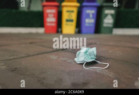 Le masque médical usagé doit être mis au rebut sur le plancher de la chaussée, sur une poubelle ou un bac de recyclage flou. Élimination des déchets médicaux sans hygiène. Masque facial avec contour d'oreille jetable Banque D'Images