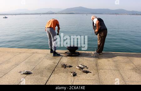 Deux pêcheurs regardant vers le bas tôt matin pêche avec la canne et la ligne dans la baie de Santander Cantabria Espagne Banque D'Images