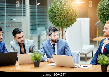 Les jeunes politiciens mènent des négociations sur un nouveau projet, un nouveau contrat, en utilisant des ordinateurs portables, assis sur une table en bois. Arrière-plan Office Banque D'Images