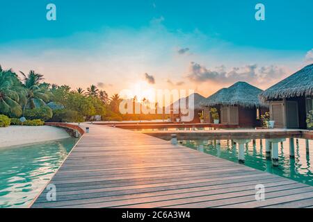 Paysage de voyage incroyable. Coucher de soleil sur l'île des Maldives, complexe de villas de luxe sur l'eau et jetée en bois. Ciel et nuages magnifiques et arrière-plan de la plage Banque D'Images