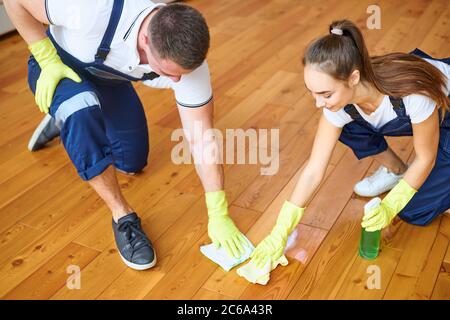 Deux nettoyants en uniformes bleus pour polir le plancher en bois avec un chiffon, nettoyer soigneusement le plancher en bois Banque D'Images