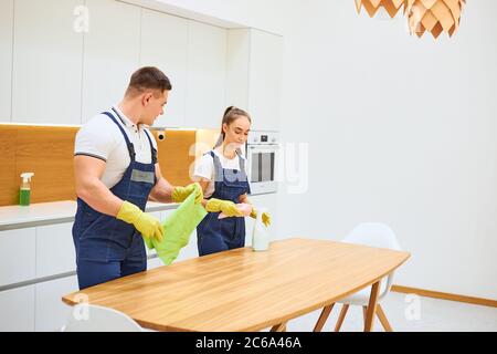 Jeunes travailleurs caucasiens du service de nettoyage travaillant dans la cuisine ensemble, essuyant la poussière de la table. Cuisine blanche Banque D'Images