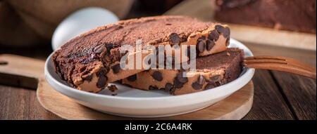 Gâteau éponge traditionnel taïwanais au goût de chocolat (taïwanais castella kasutera) sur une table de fond en plateau de bois avec les ingrédients, gros plan. Banque D'Images