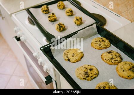 Deux plaques de cuisson sur la table de cuisine - avec des biscuits américains cuits et des boules de pâte crues. Banque D'Images