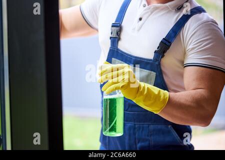 Un type court musclées en uniforme du service de nettoyage portant des gants de protection jaunes, tenant le spray de lavage de la fenêtre Banque D'Images