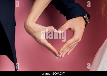 Portrait gros plan mains de couple en formation d'amour entendre isolé sur fond rose. Homme en tuxedo Banque D'Images