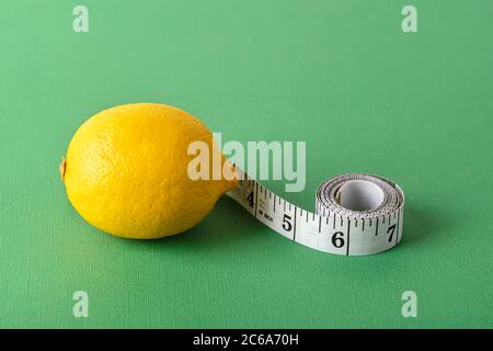 Ruban de mesure de pouce et citron jaune mûr sur fond vert. Concept de saine alimentation, régime, perte de poids et corps mince. Copier l'espace. Banque D'Images