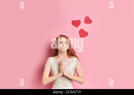 Portrait de la belle femme portant en robe blanche rêve sur l'amour vrai, avec les coeurs rouges au-dessus de la tête. Isolé sur fond rose Banque D'Images