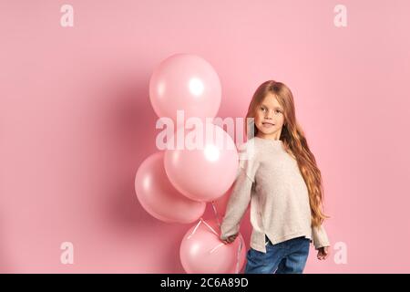 Portrait de drôle de caise fille de enfant avec des ballons d'air roses, les cheveux longs et les grands beaux yeux, portant blouse blanche et jeans. Banque D'Images