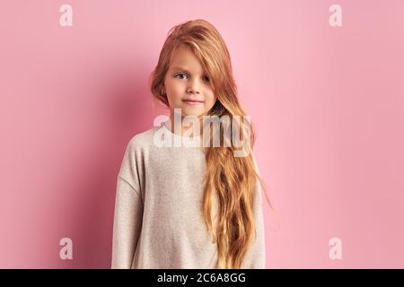 Belle fille de caucasien apparence avec de longs cheveux dorés, grands beaux yeux charmants, portant le chemisier blanc regarder l'appareil photo isolé sur le dos rose Banque D'Images