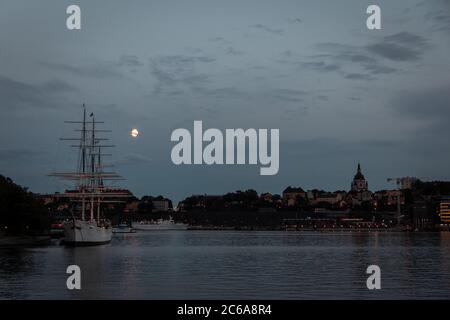 Vue nocturne sur l'eau à Stockholm avec un bateau et la pleine lune visible Banque D'Images