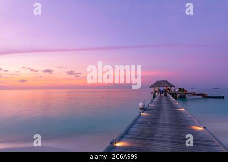 Paysage de coucher de soleil incroyable aux Maldives. Villas de luxe avec vue sur mer et lumières LED sous un ciel coloré. Un voyage de luxe tranquille Banque D'Images