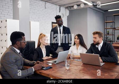 Jeune femme caucasienne aux cheveux rouges vêtue d'un costume formel tenant une réunion avec un groupe multiethnique de personnes impliquées dans le commerce. Concept d'entreprise Banque D'Images