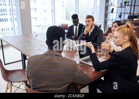 Jeune femme caucasienne aux cheveux rouges vêtue d'un costume formel tenant une réunion avec un groupe multiethnique de personnes impliquées dans le commerce. Concept d'entreprise Banque D'Images