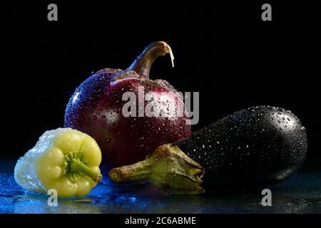 Deux aubergines et poivrons verts, humides sur fond noir avec un reflet Banque D'Images