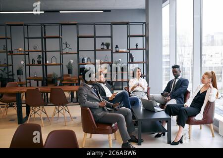 Un groupe de partenaires d'affaires interprofessionnels discute de l'avenir réussi dans le bureau moderne, portant des vêtements formels Banque D'Images