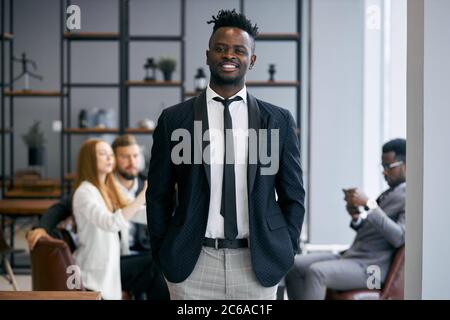 Homme d'affaires souriant portant un support en tuxedo classique posé dans un environnement de bureau et regarder positivement la caméra. Concept de personnel d'affaires. Partenaire commercial Banque D'Images