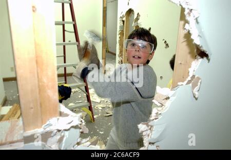 Austin Texas États-Unis, 2003 : un garçon de huit ans portant des lunettes de sécurité utilise un marteau de traîneau pour aider à briser les cloisons sèches sur le projet de rénovation de bureau. Modèle validé. ©Bob Daemmrich Banque D'Images