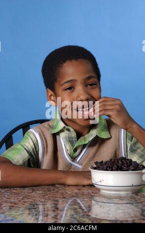 Austin, Texas États-Unis, décembre 2003 : garçon afro-américain de huit ans mangeant des raisins secs à la maison. MR ©Bob Daemmrich Banque D'Images