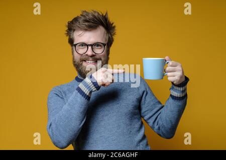 Drôle, heureux homme pointe l'index à une tasse de boisson chaude, l'offrant à des amis. Banque D'Images