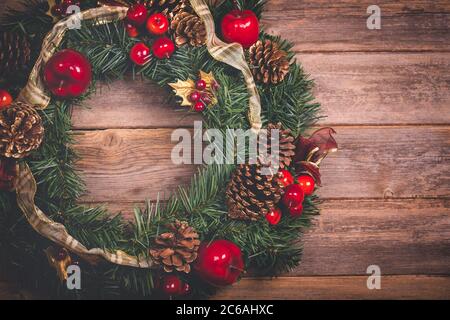 Photo rétro d'une couronne de Noël, avec rubans, cônes de sapin, pommes et baies, sur fond de bois ancien. Filtré et mis en tons pour ressembler à et o Banque D'Images