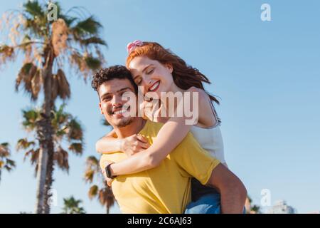 le jeune homme porte sa petite amie sur le dos tout en souriant Banque D'Images