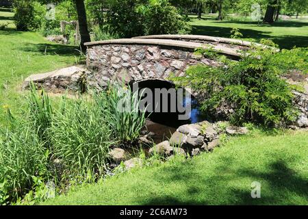 un ruisseau de campagne qui traverse un pont de mur de roche avec des feuillages luxuriants et des ombres Banque D'Images