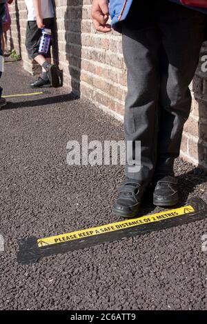 Enfant d'école primaire debout sur la ligne de distance sociale pendant l'épidémie Covid-19 de 2020, Angleterre Banque D'Images