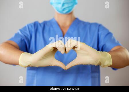 Médecin dans un masque facial et des gants formant un coeur devant une chemise bleue, Banque D'Images