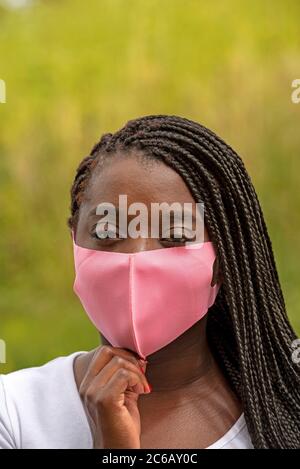 Angleterre, Royaume-Uni. 2020. Portrait d'une femme noire avec un style de cheveux tressé et portant un masque rose pendant l'épidémie de Covid-19 Banque D'Images