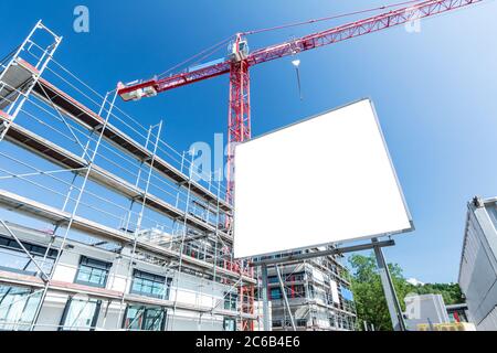 Panneau d'affichage vierge sur un chantier de construction avec construction non achevée, échafaudage et grue Banque D'Images