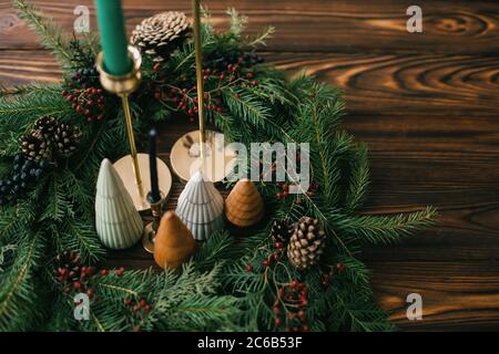 Arbres de Noël et bougies dans une couronne de noël rustique sur bois sombre. Décoration moderne festive. Joyeuses vacances. Pins miniatures, chandeliers et moder Banque D'Images