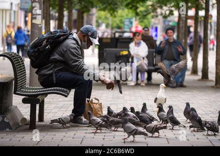 Glasgow, Écosse, Royaume-Uni. 8 juillet 2020. Photo : un homme nourrit les pigeons à la main dans la rue Sauchielhall du quartier commerçant de Glasgows. Crédit : Colin Fisher/Alay Live News Banque D'Images