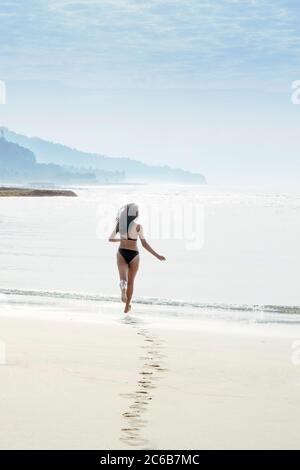 Une femme voyageant seule dans un bikini courant dans la mer sur une plage tropicale immaculée et laissant des empreintes de pieds, Indonésie, Asie du Sud-est, Asie Banque D'Images